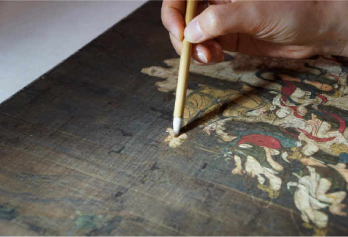 菩薩の衣を描いた白い絵具に筆で膠水溶液を浸透させる。絵具は接着力が低下しており、至急処置が必要だった。※資料提供：岡墨光堂