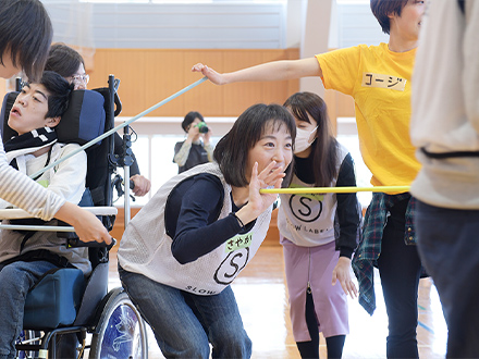 【写真4】道具を使ったコミュニケーションの学習。二人でペアになり、互いの掌（てのひら）で棒の端を相手に向けて押し合いながら、棒を落さずに運ぶワーク。