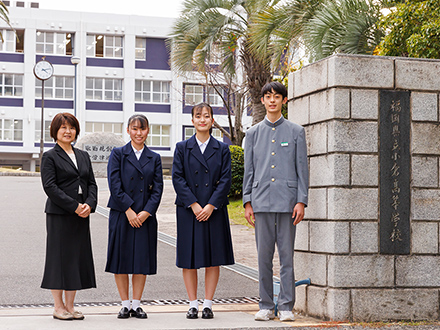 学校の正門前で。左から探究活動推進課長の徳永教諭、2年生の原さん、佐々木さん、1年生の井上さん