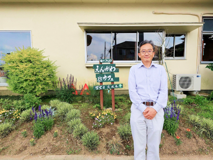 美しい花々に彩られた「えんがわハウス」の前に立つ横田代表理事。
