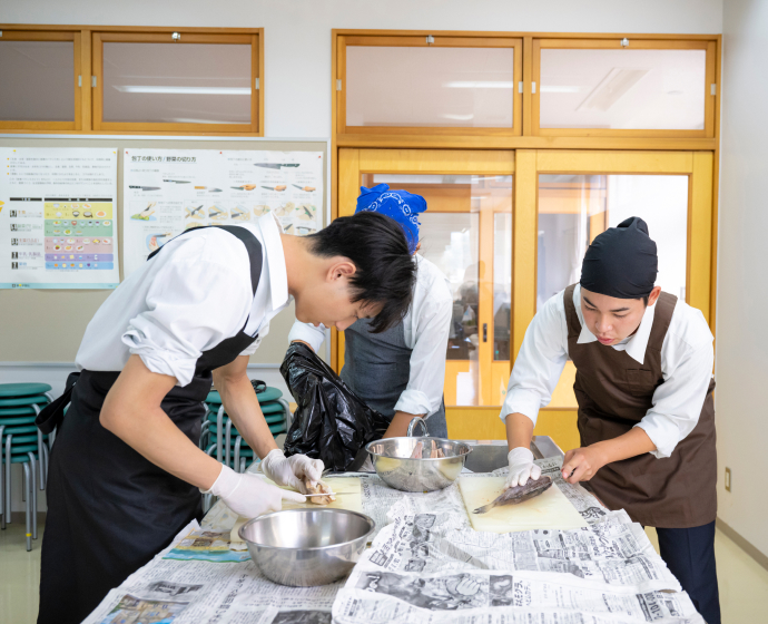 メンバーの1人、中村翔生(なかむら・とき)さん(写真右)のレクチャーにより全員がテキパキと魚をさばき、調理する。